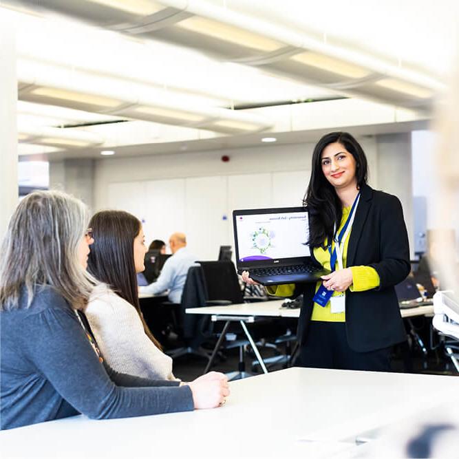 Professional woman in an office environment, showing a presentation slide on a laptop screen to colleagues