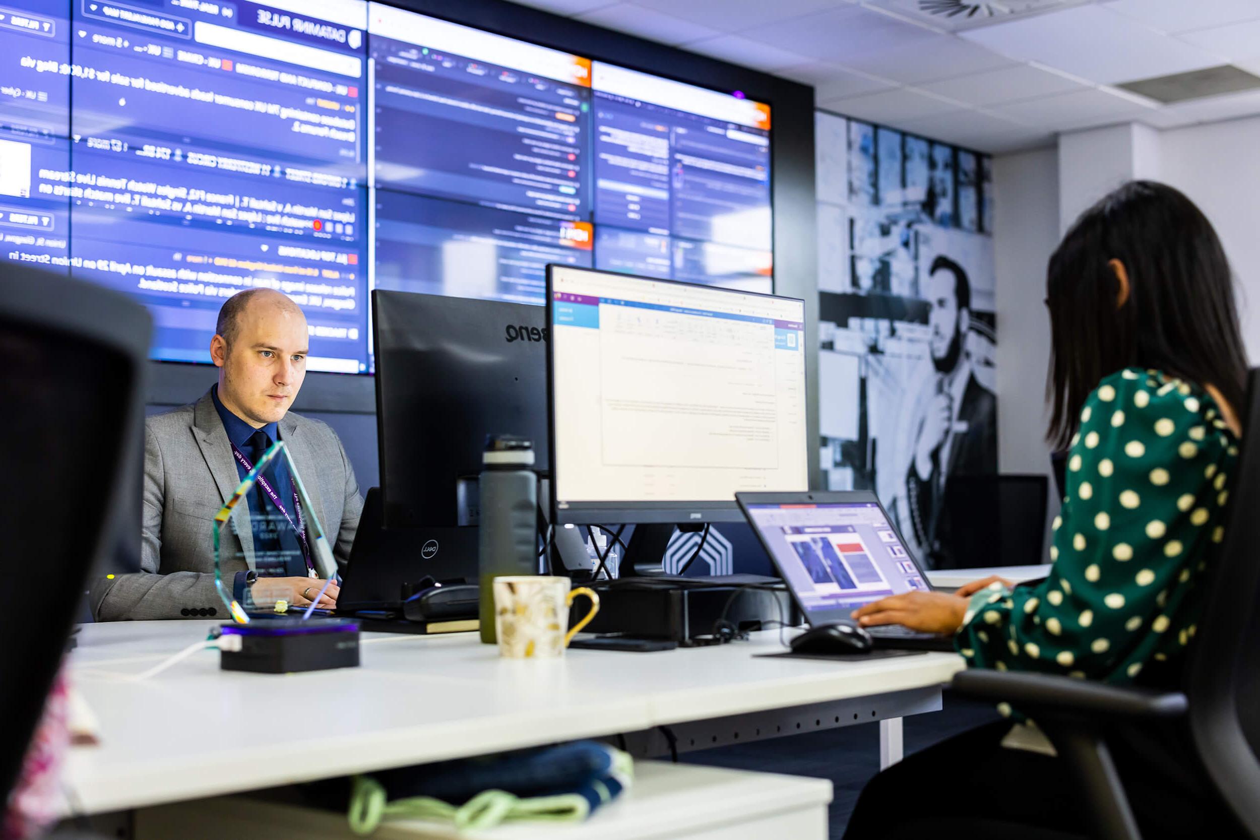 Desk staff using computers for Mitie Intelligence, with screens on the walls